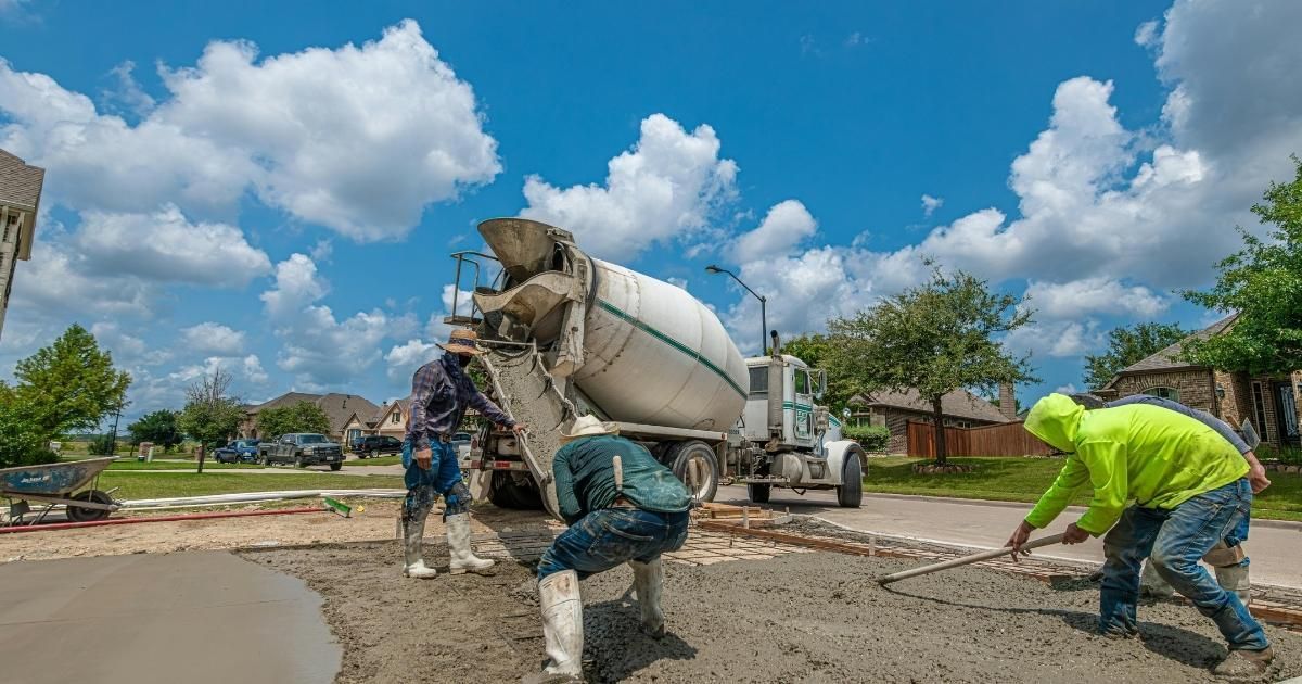 Concrete being poured from a cement truck onto a driveway, with workers smoothing it out under a bright blue sky.