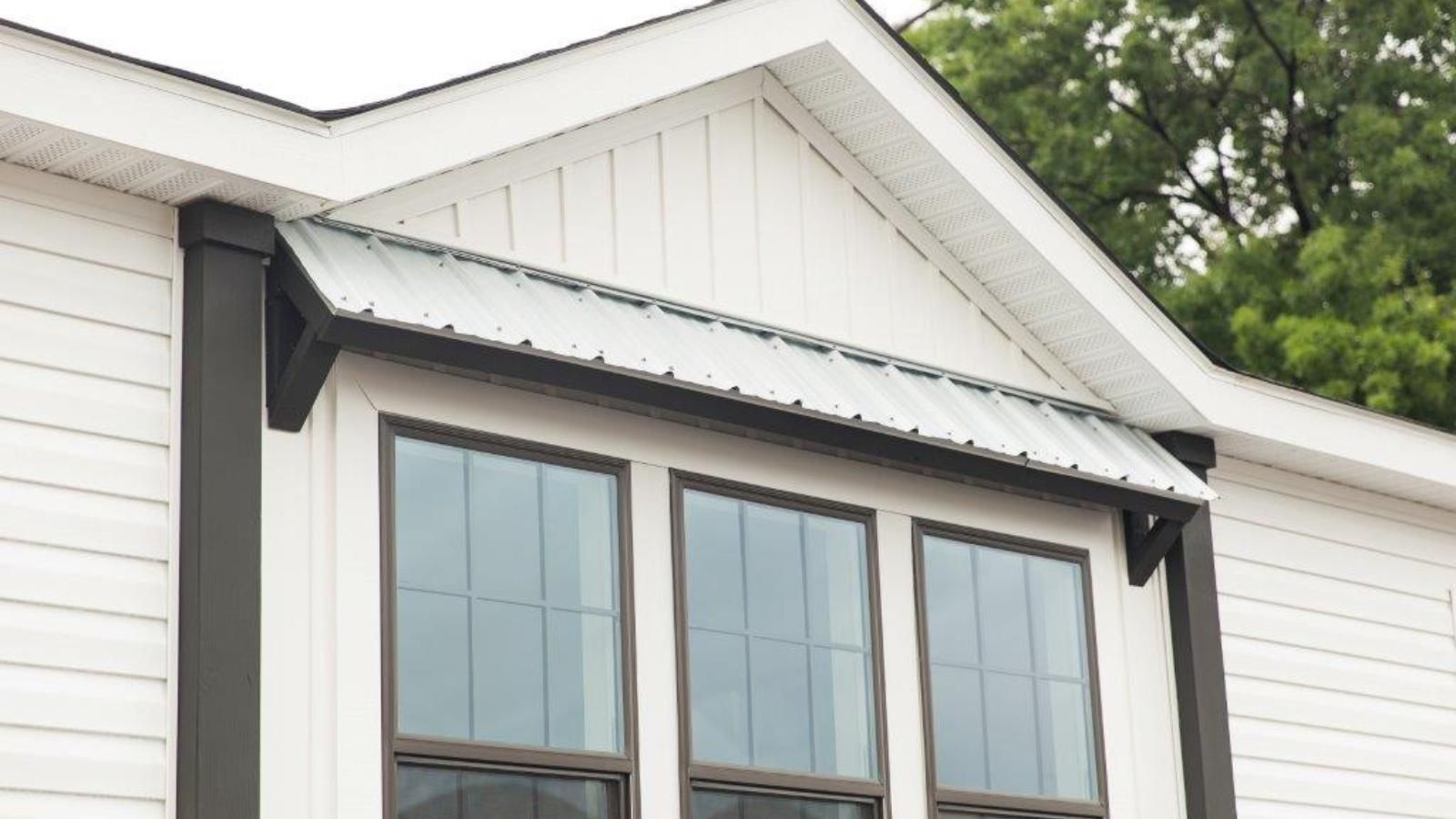 A white manufactured home with three windows and a metal roof.