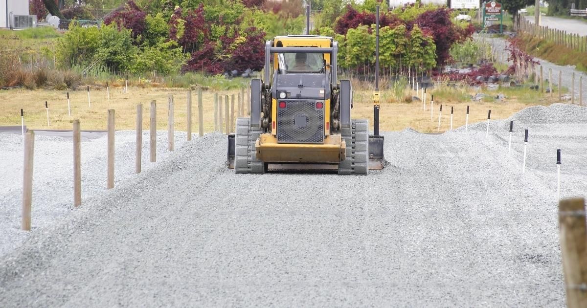 Yellow bulldozer leveling gravel on a construction site, with wooden stakes marking boundaries.