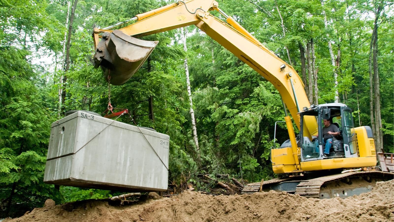 A yellow excavator is lifting a large septic tank.