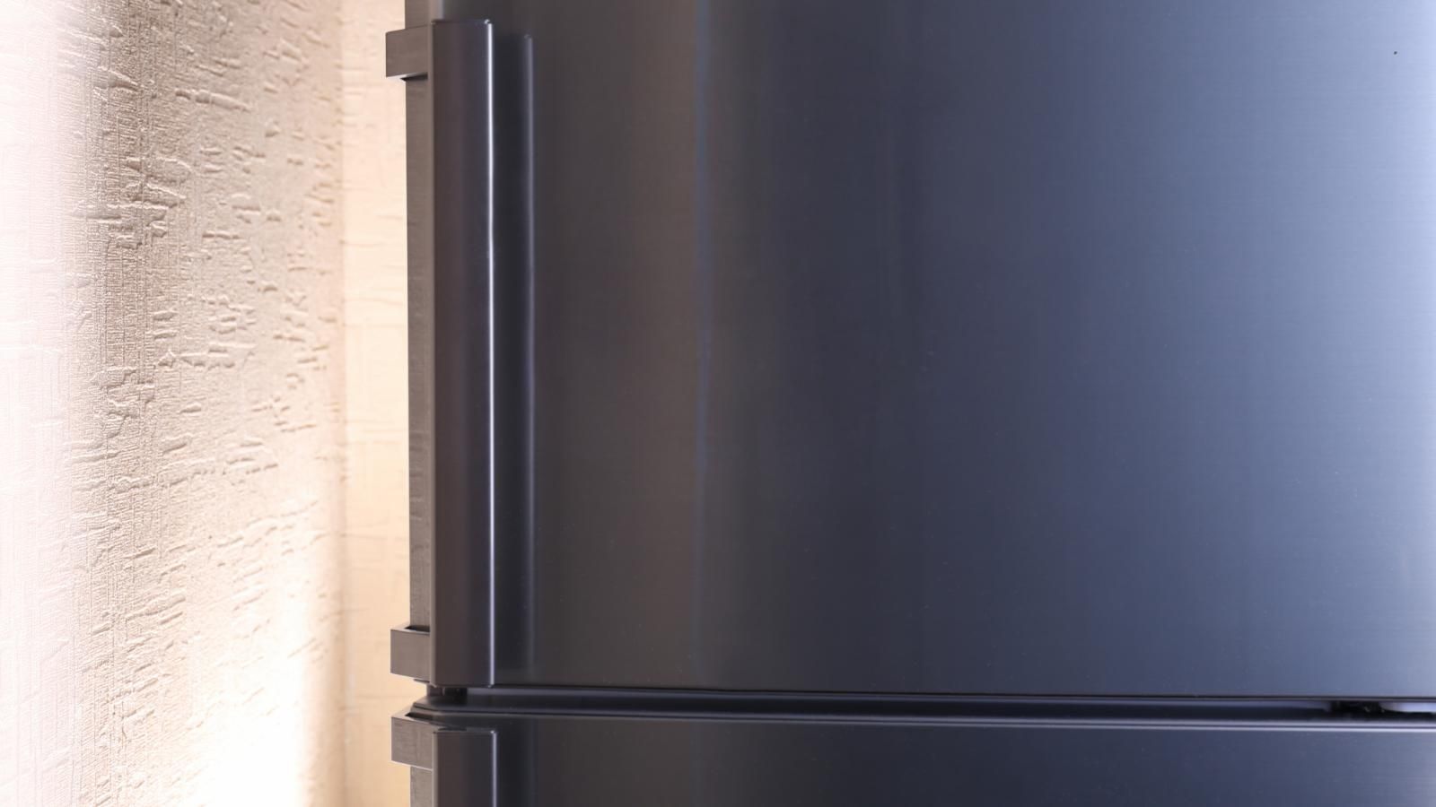 A black refrigerator is sitting next to a white wall.