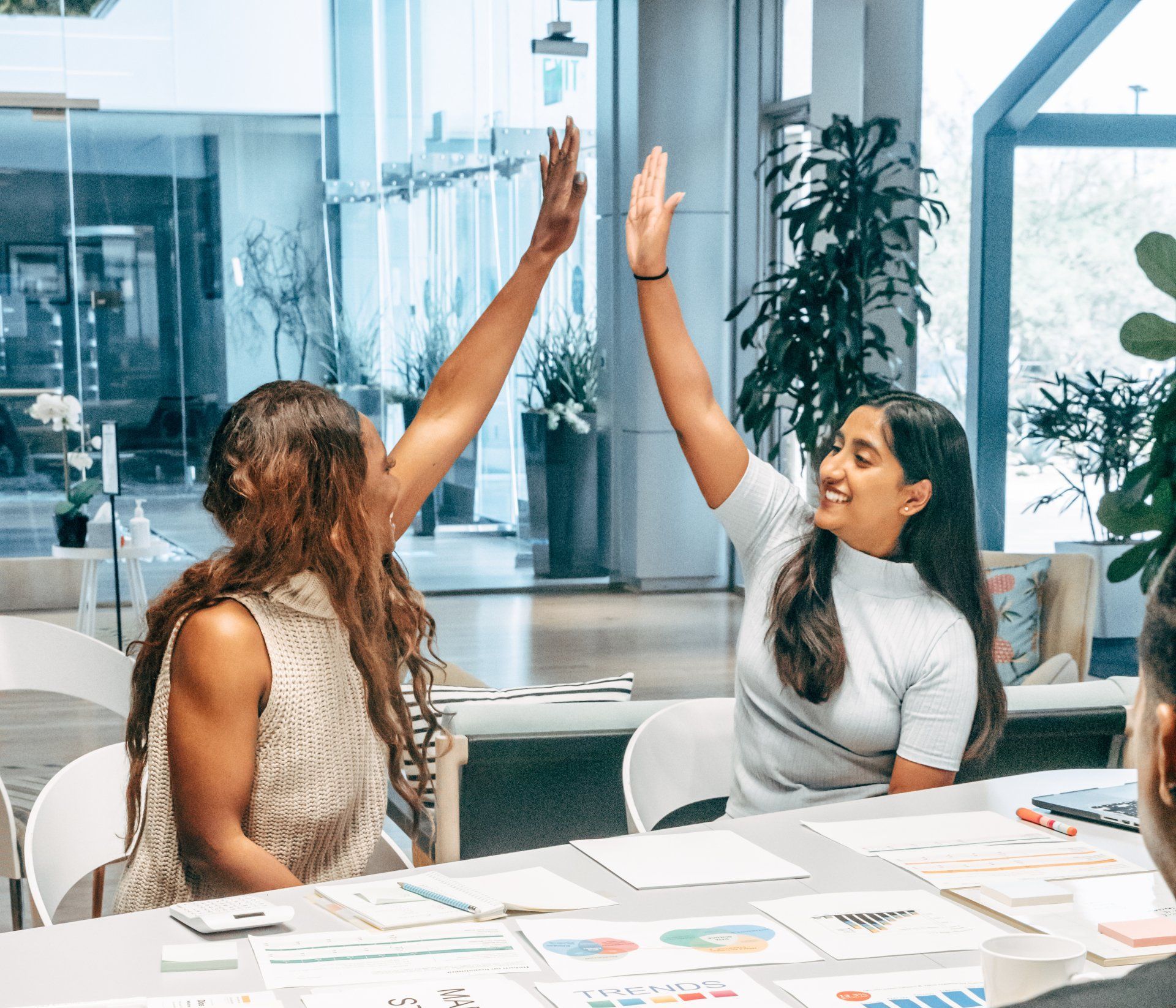 Two women are giving each other a high five while sitting at a table.