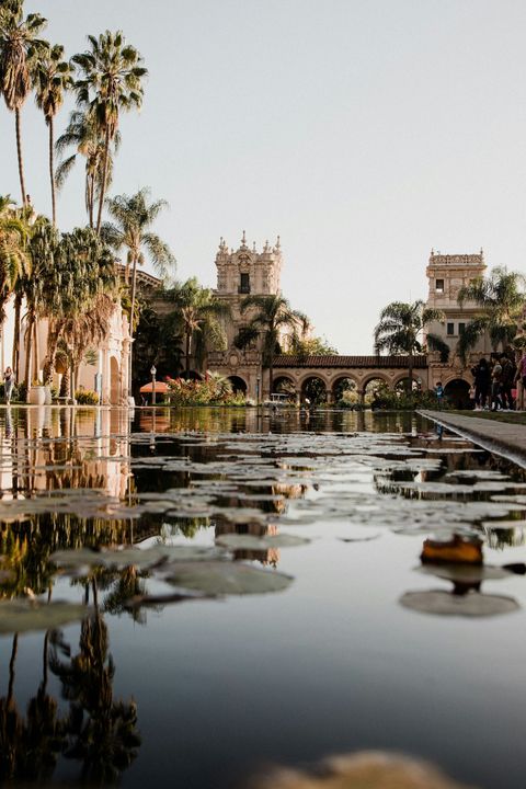 Reflection of ornate Spanish-style buildings and palm trees in a calm water pool in San Diego, CA.