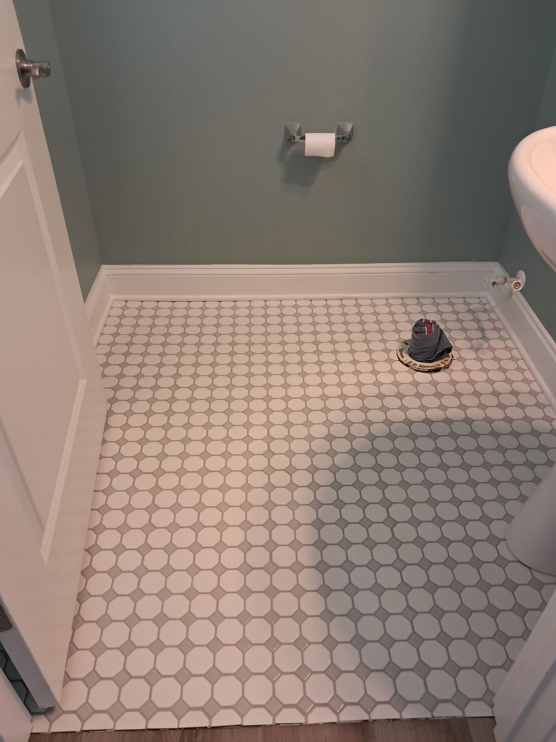 Small bathroom with white circle tile floor and sage green walls.
