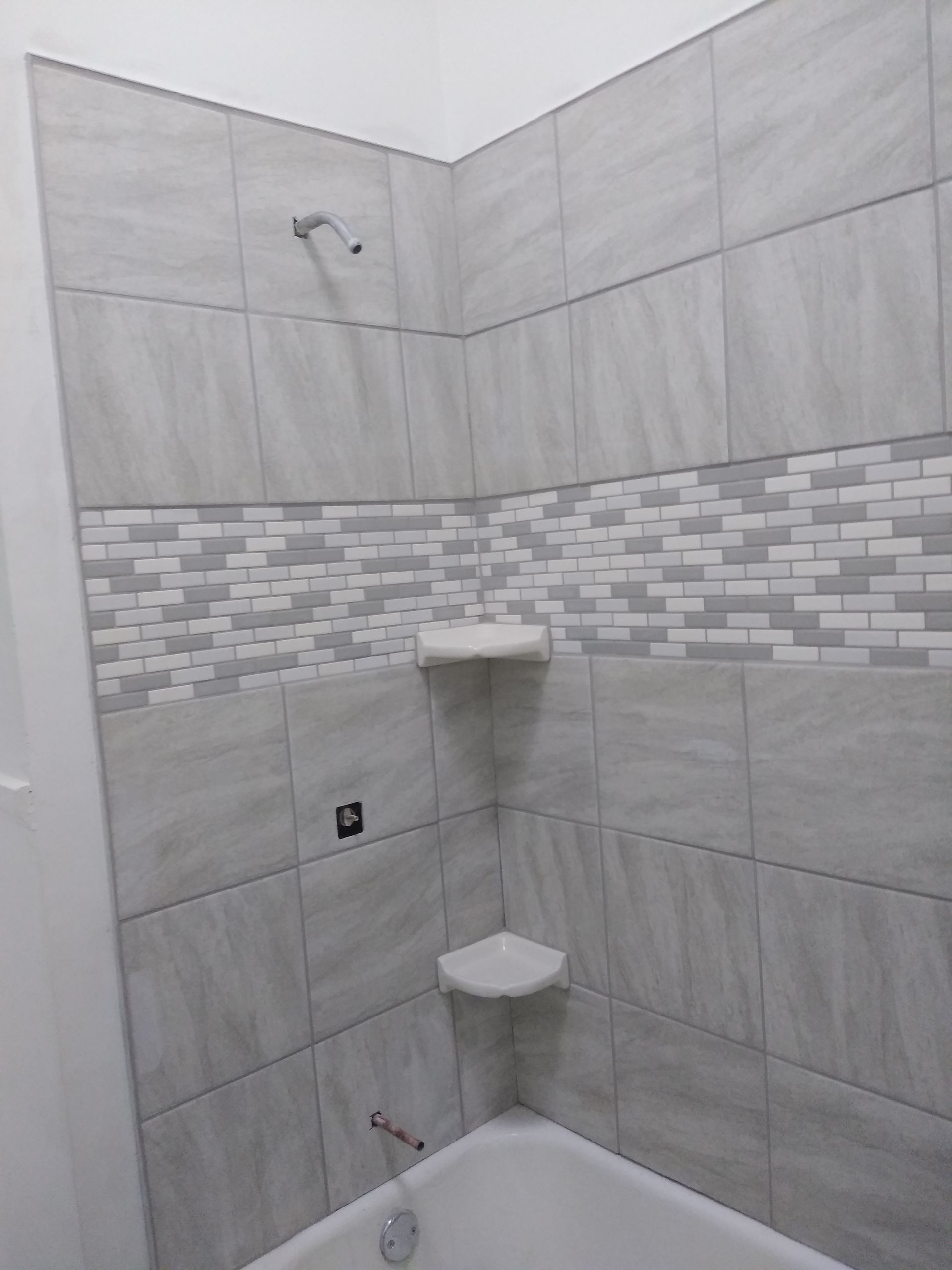Bathroom corner with gray tiled walls, decorative accent, showerhead, and bathtub.