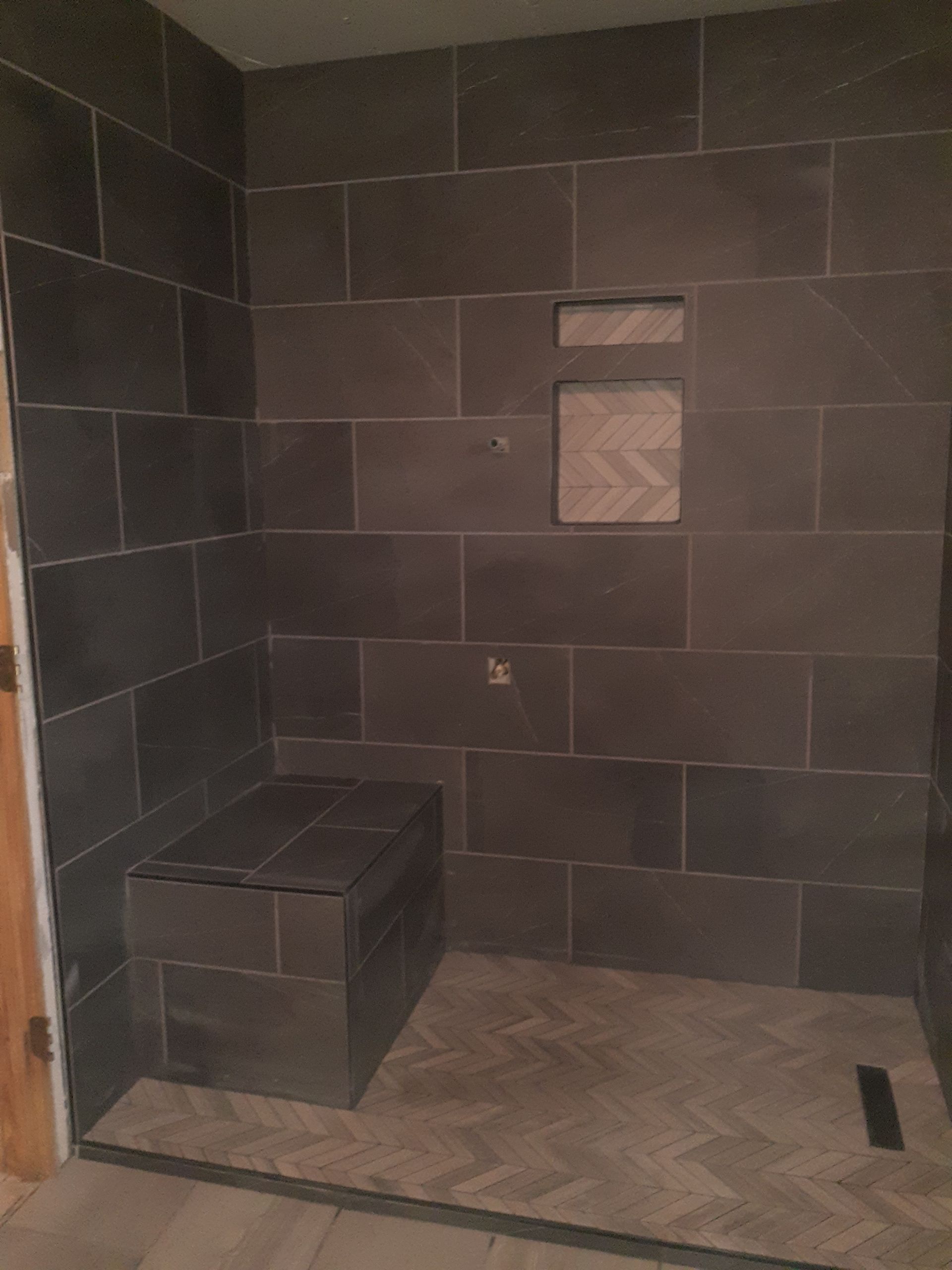 Dark gray tiled shower with built-in bench and niche. Herringbone tile floor.