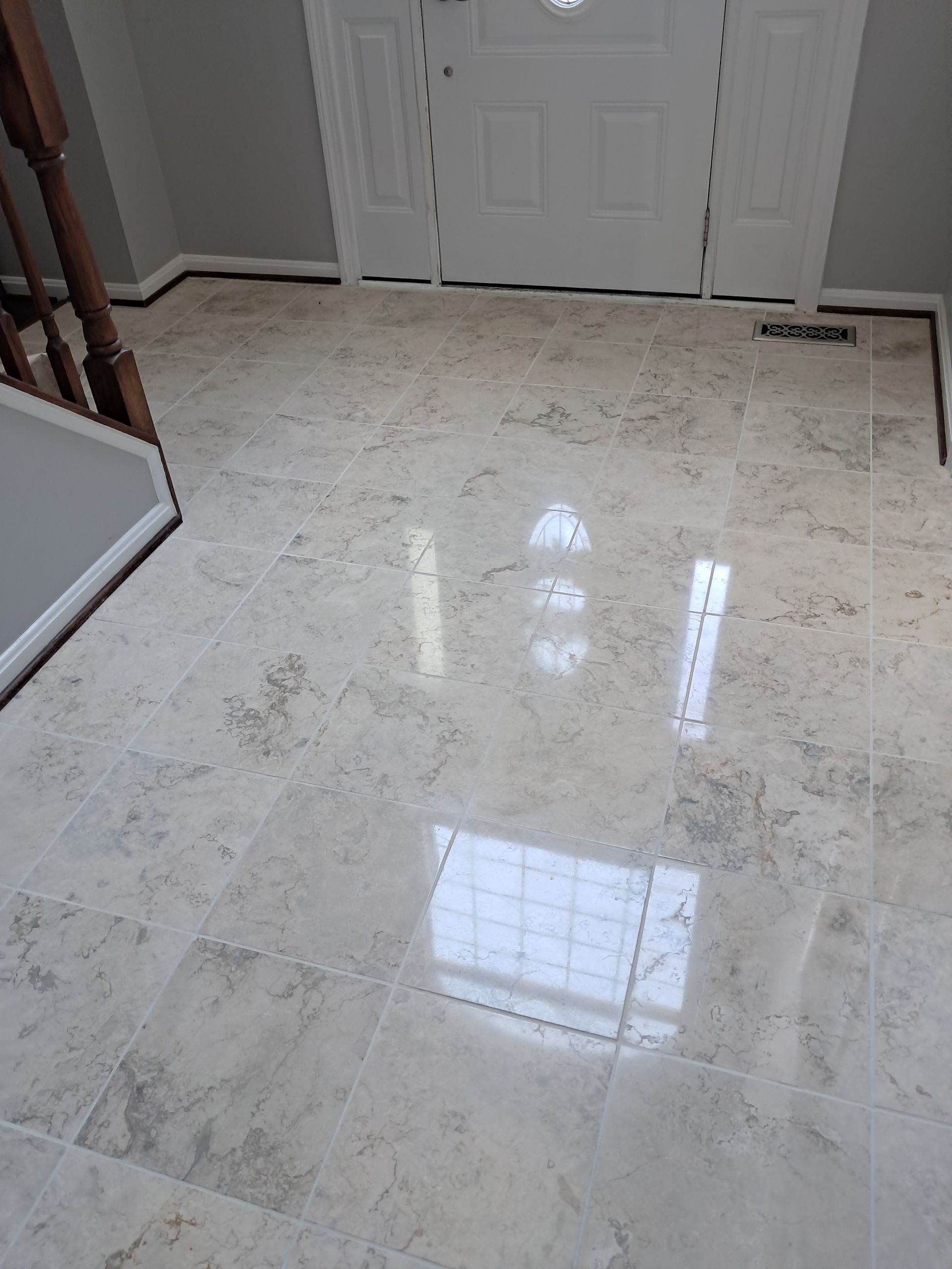 Light-colored tiled floor reflecting light in an entryway, with a white door in the background.