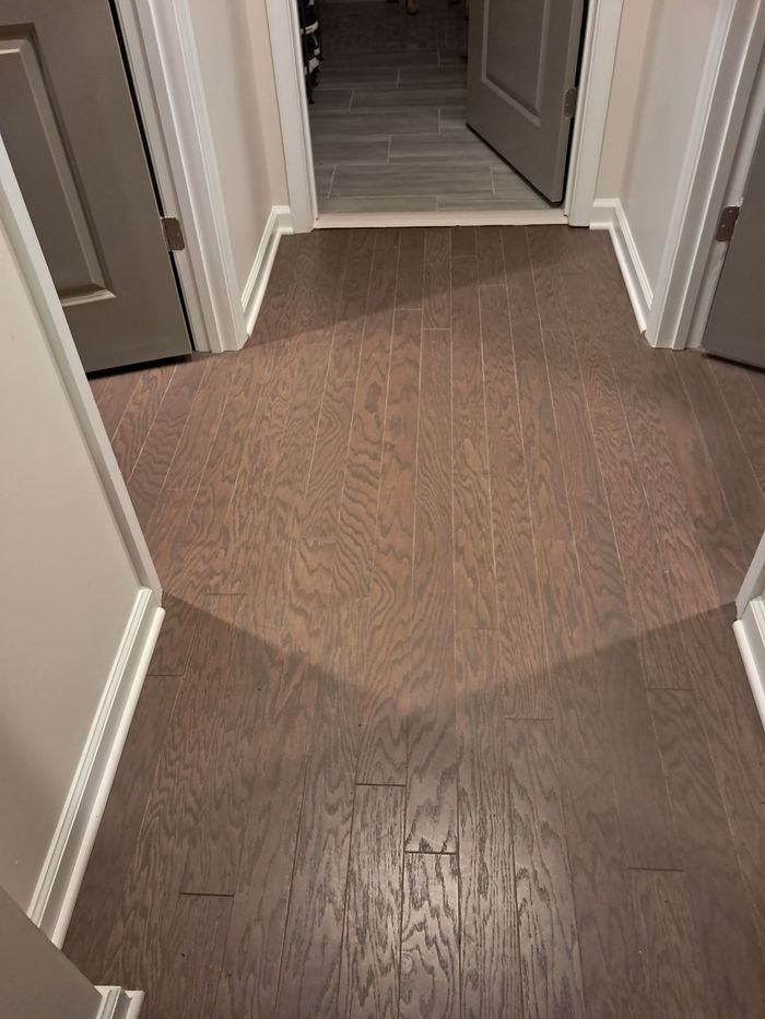 Brown hardwood floor in a hallway with white trim and doors.