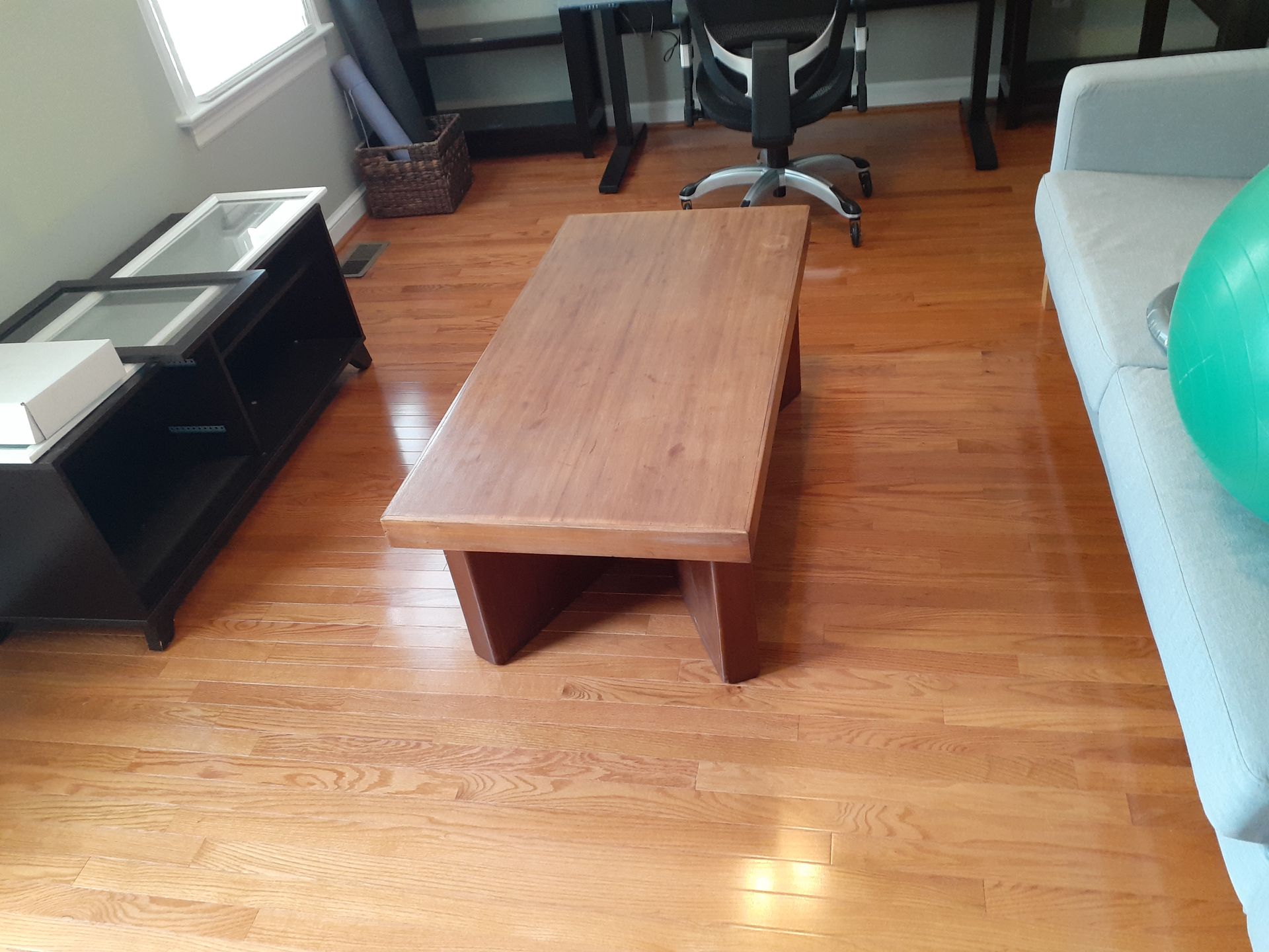 Wooden coffee table on hardwood floor, with black media console and gray sofa visible in the background.
