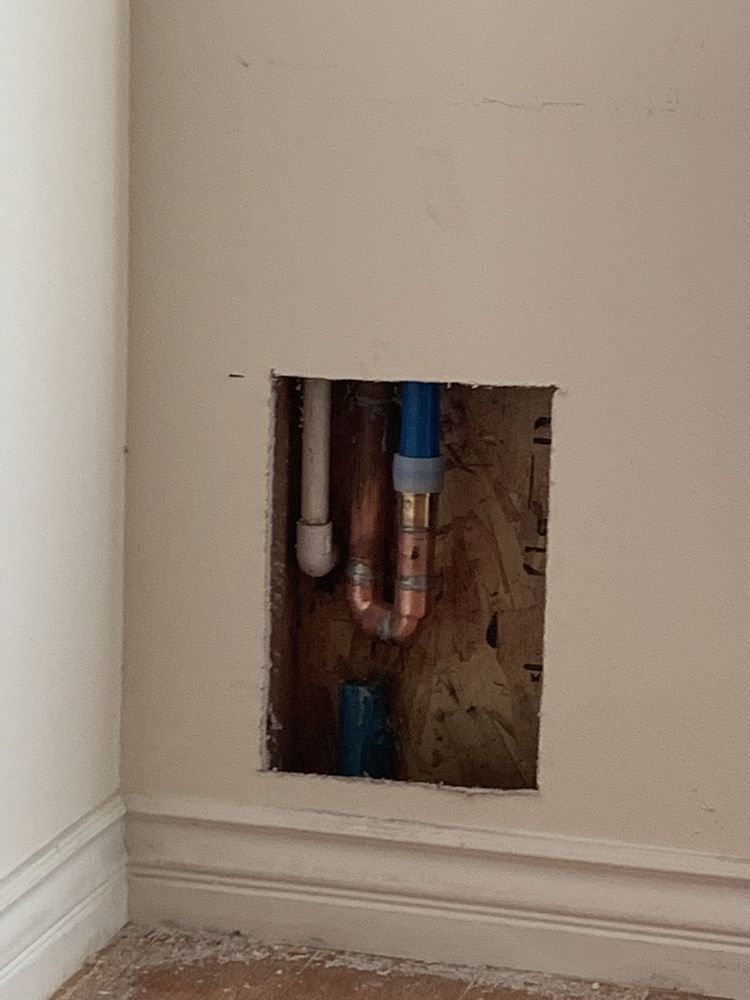 A hole in a wall with copper pipes coming out of it.