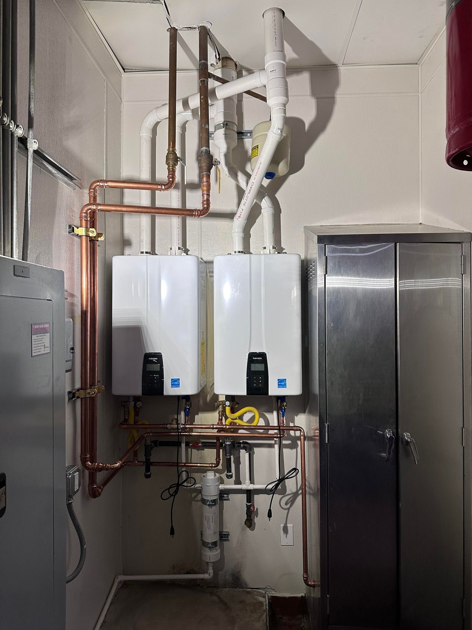 A room with two water heaters and copper pipes.