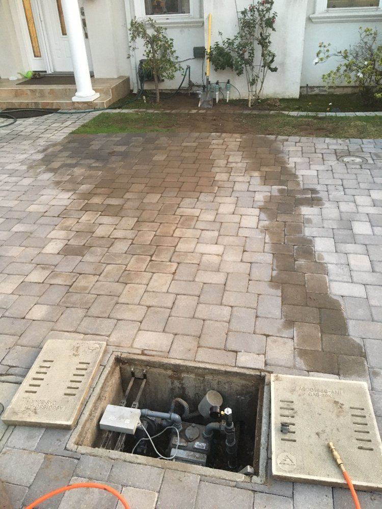 A hose is coming out of a hole in a brick driveway.