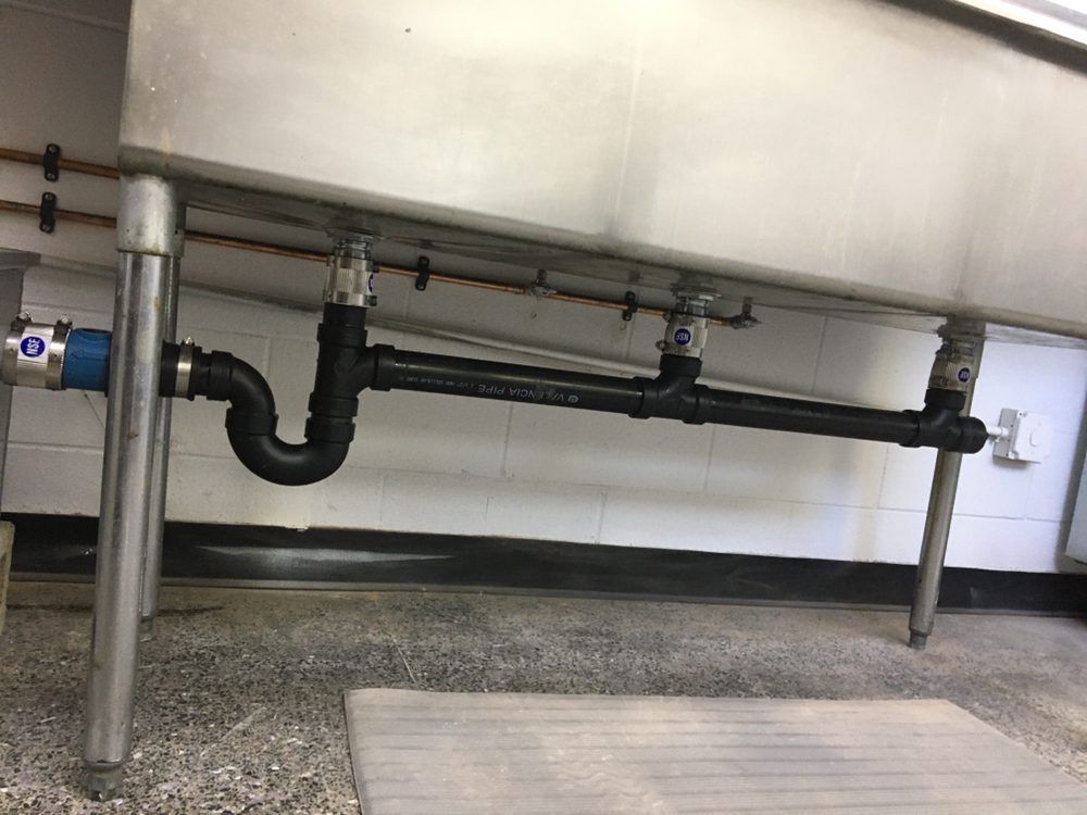 A stainless steel sink with black pipes attached to it.