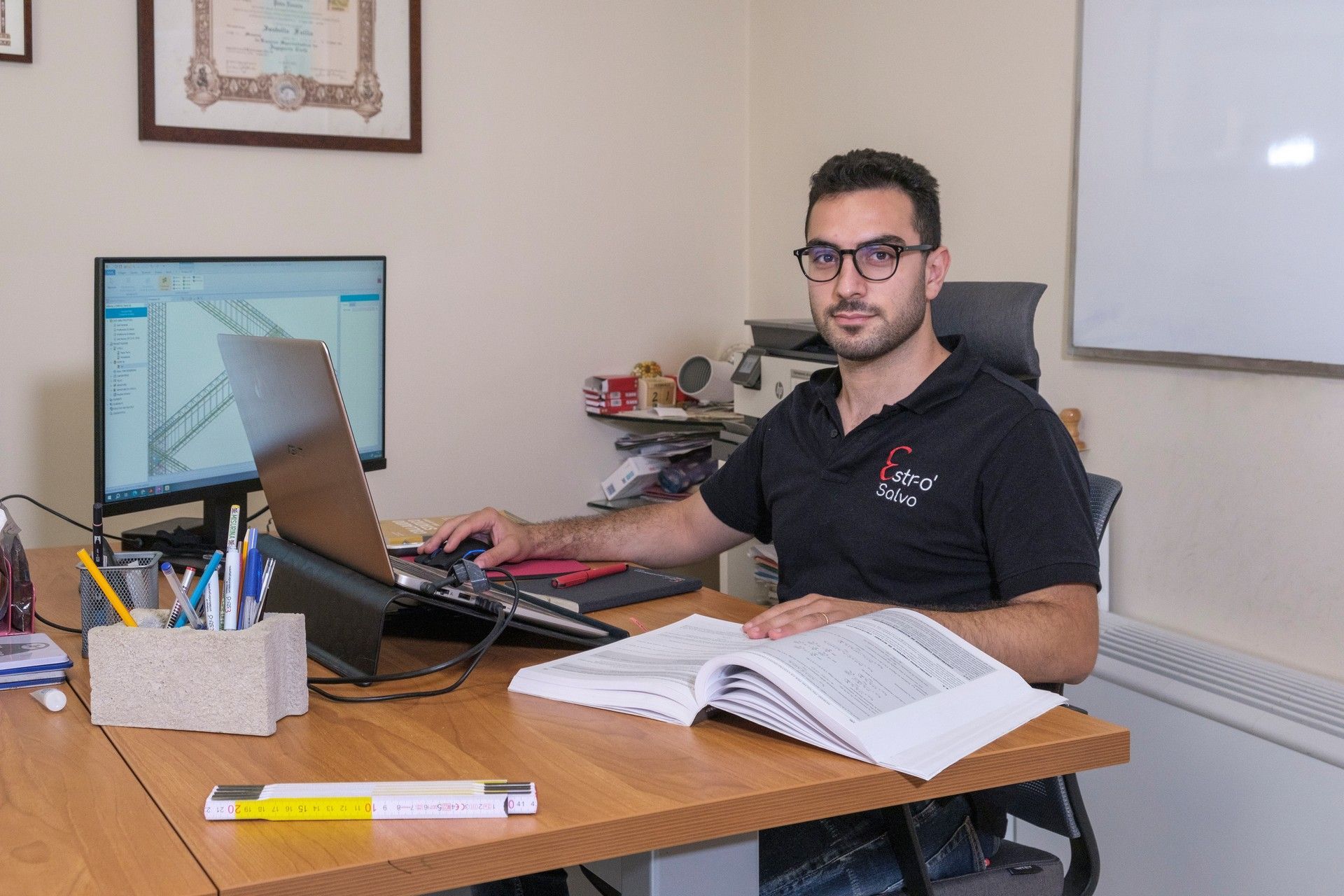 Un uomo è seduto alla scrivania con un computer portatile e un libro.