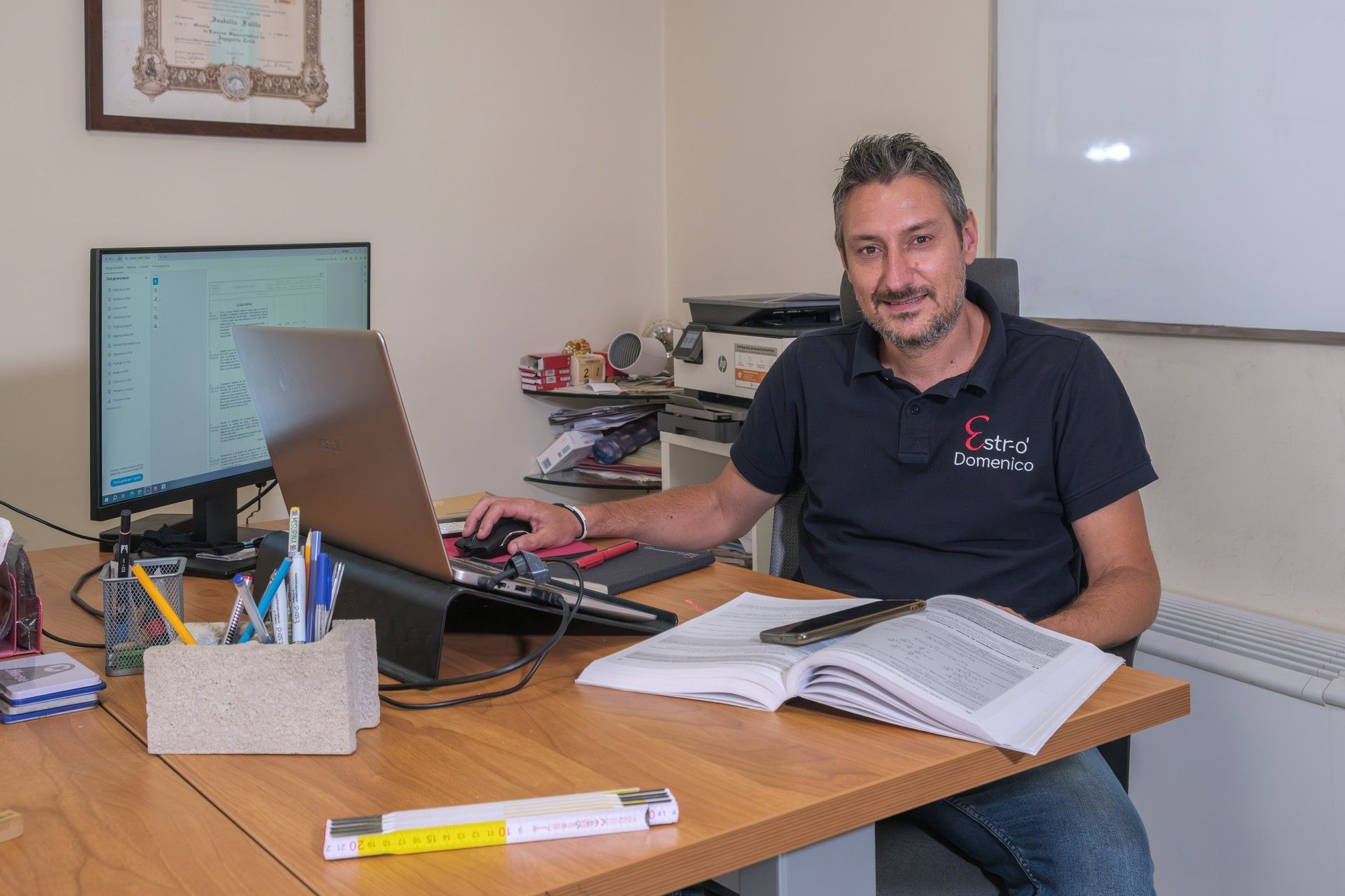 Un uomo è seduto alla scrivania con un computer portatile e un libro.