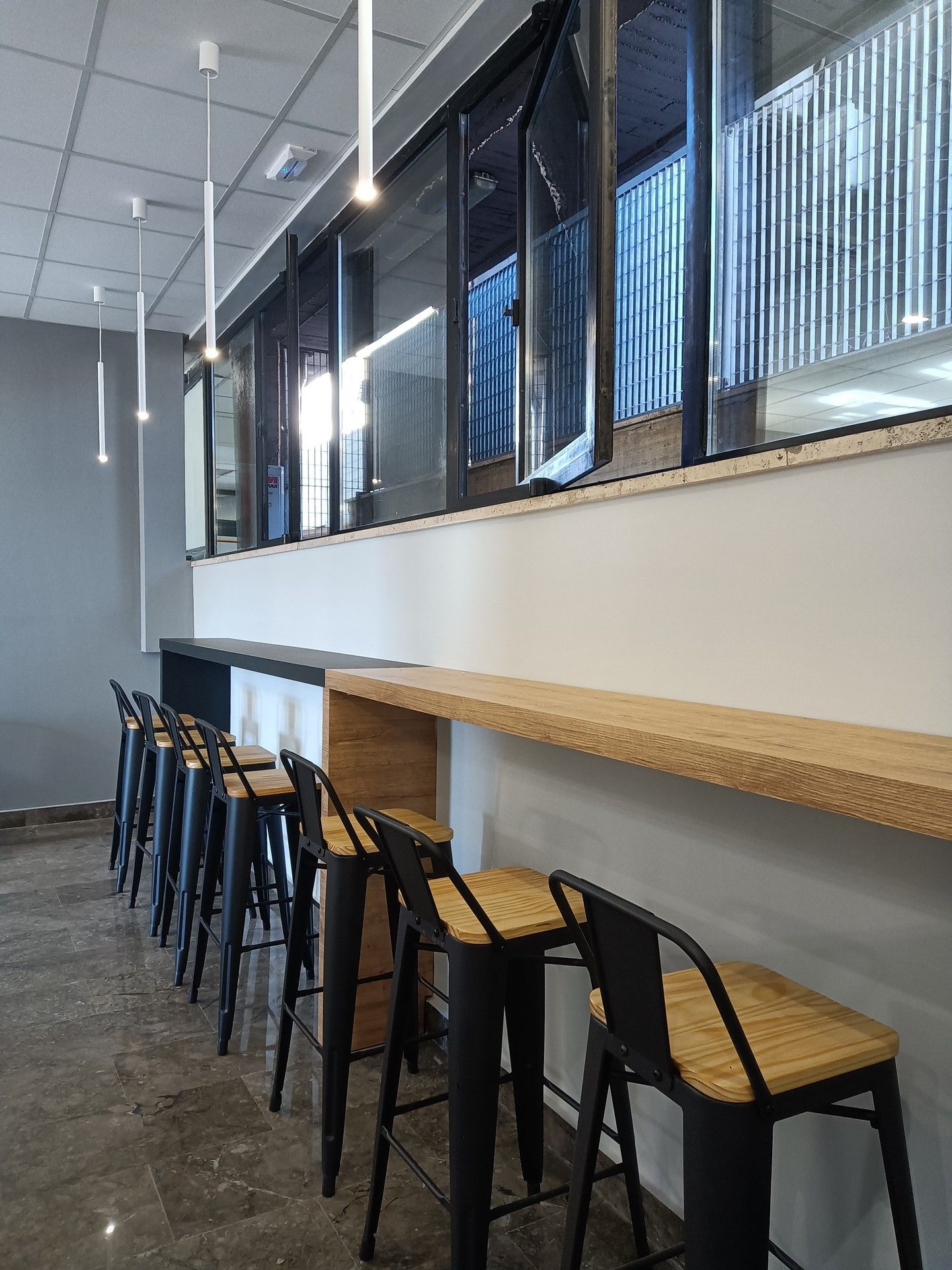 Una fila di sgabelli da bar sono allineati in una stanza accanto a una finestra.