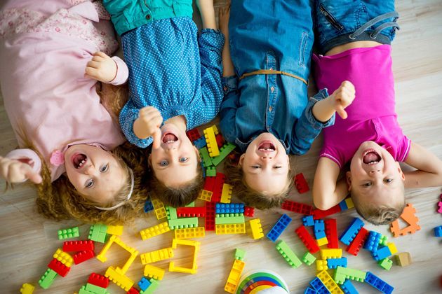 Quatre enfants allongés sur un tapis, entourés de blocs de construction colorés, regardent l'objectif.