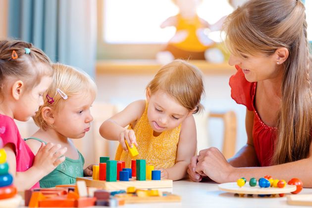 Un adulte guide des enfants dans une salle de classe lumineuse pendant qu'ils jouent avec des blocs et des jouets colorés.