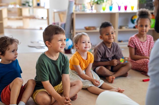 Des enfants assis en tailleur sur le sol d'une salle de classe, regardant ou écoutant ensemble
