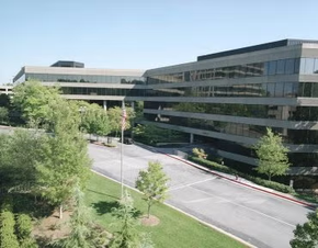 Modern office buildings beside a tree-lined road on a sunny day