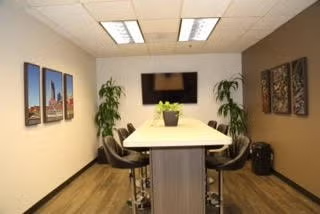 Modern conference room with a long table, black chairs, wall art, plants, and a mounted TV.