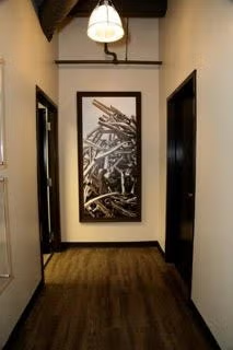 Narrow hallway with dark doors, wood floor, ceiling light, and abstract framed artwork on the far wall