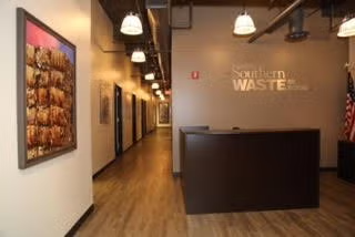Modern office lobby with a dark reception desk, hallway, pendant lights, and wood flooring