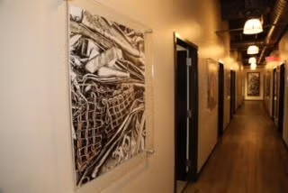 Narrow hallway with framed abstract art on cream walls and warm hanging lights over wood flooring.