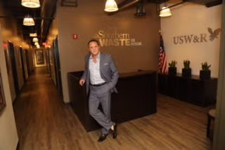 Man in a suit leaning in an office lobby with wood floors and company signage behind him