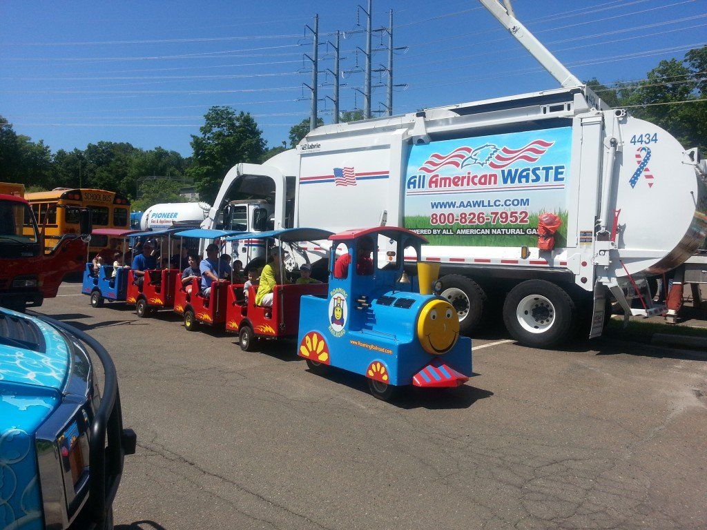 Visitors ride on a trackless train in front of a front load All American Waste truck at the Touch A Truck event