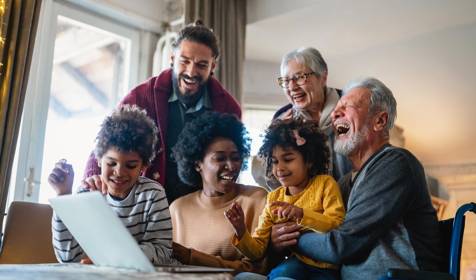 Joyful multigenerational family gathered around a laptop in a cozy living room.