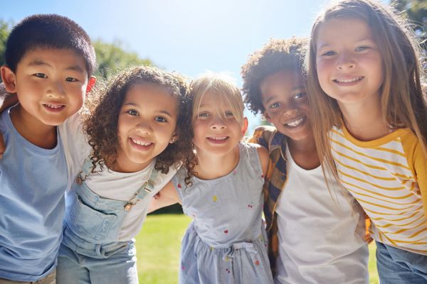 Five diverse children smiling and standing close together outdoors on a sunny day. Five diverse children smiling and standing close together outdoors on a sunny day.