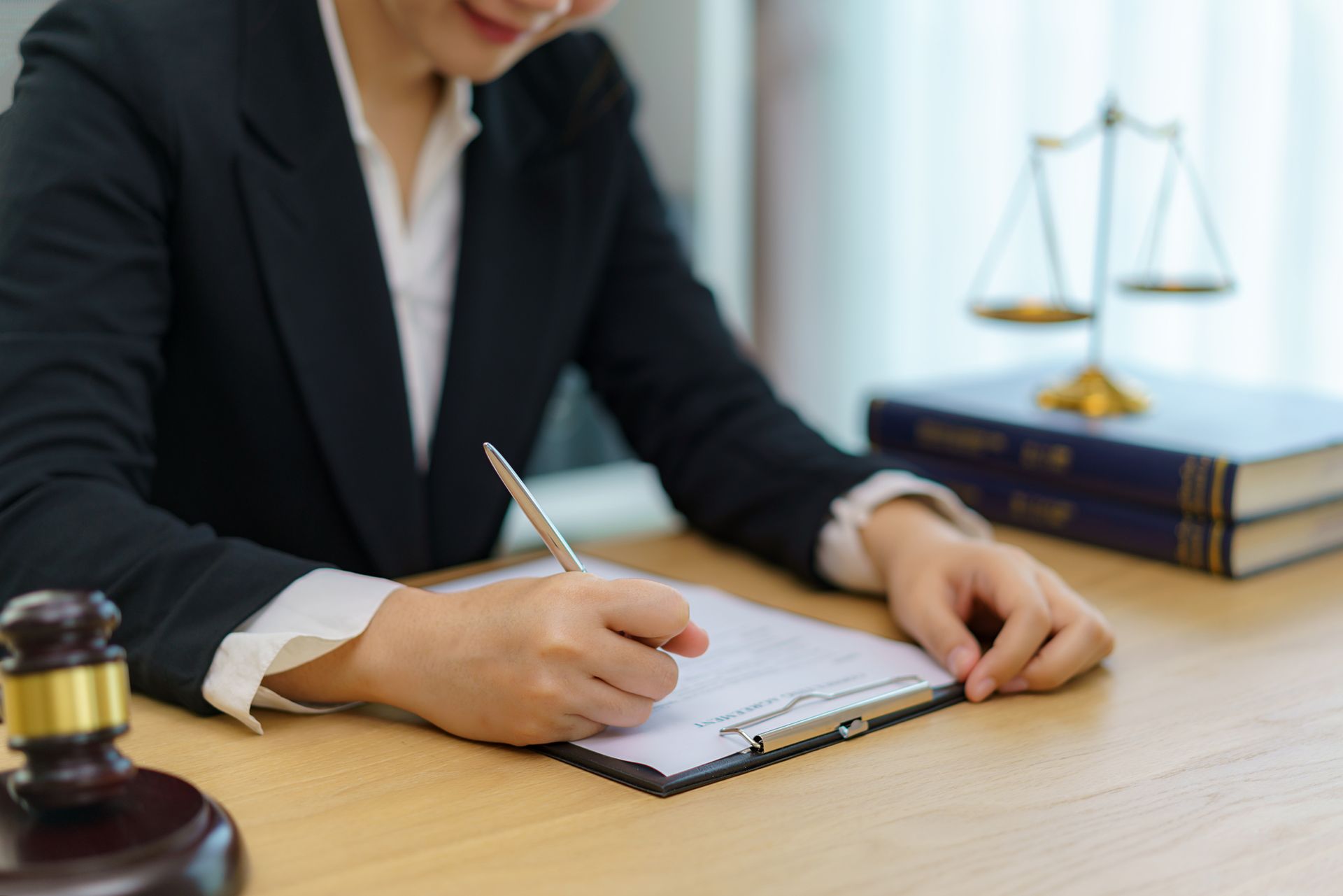 A lawyer signing documents with a wooden gavel on her desk and books with scales in the background.