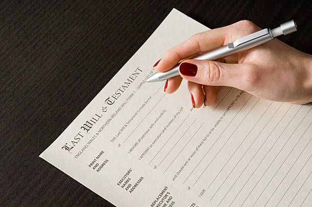 A woman with red nails filling out a last will and testament form on a dark surface using a pen