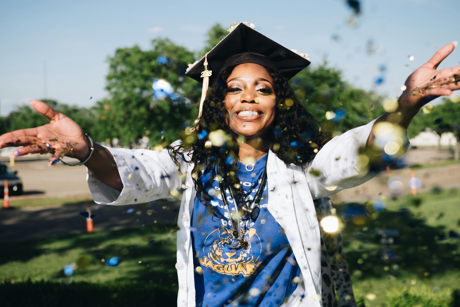 A woman in a graduation cap and gown is throwing confetti in the air.