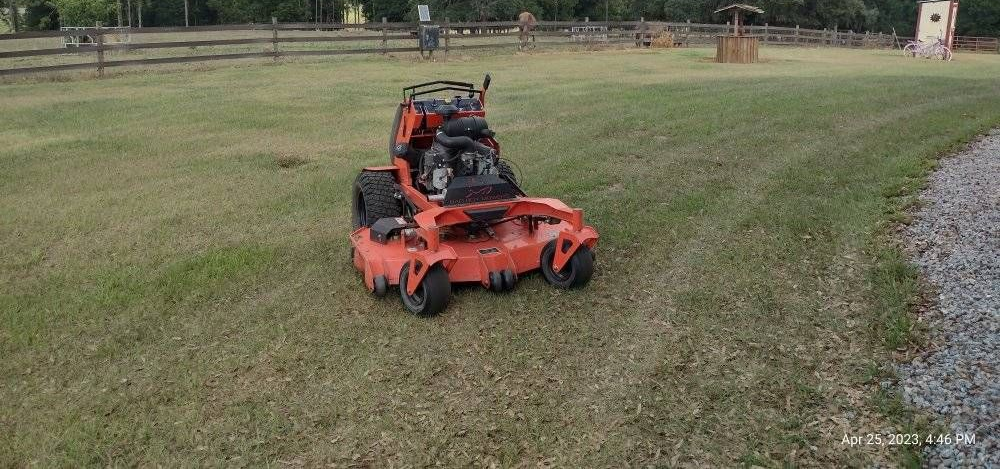 Orange riding lawnmower on a grassy field with trees and a cloudy sky.