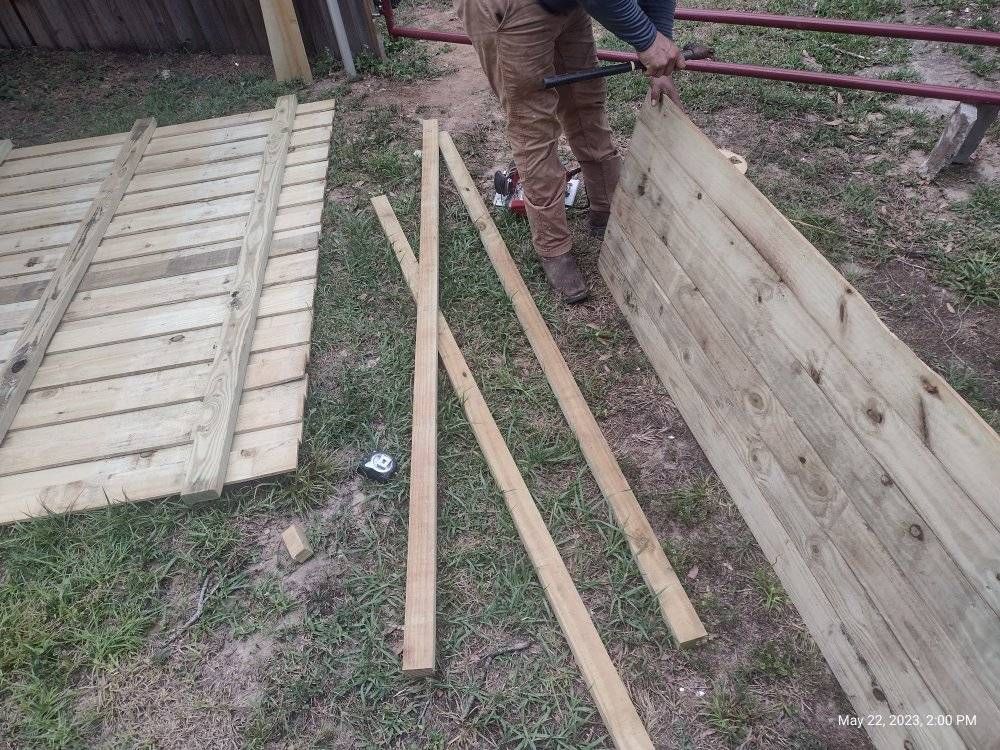 Person working with wood boards outdoors, likely constructing a structure.
