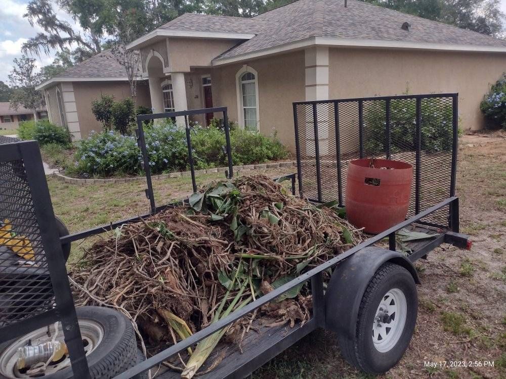 Trailer filled with yard waste, parked in front of a tan house.