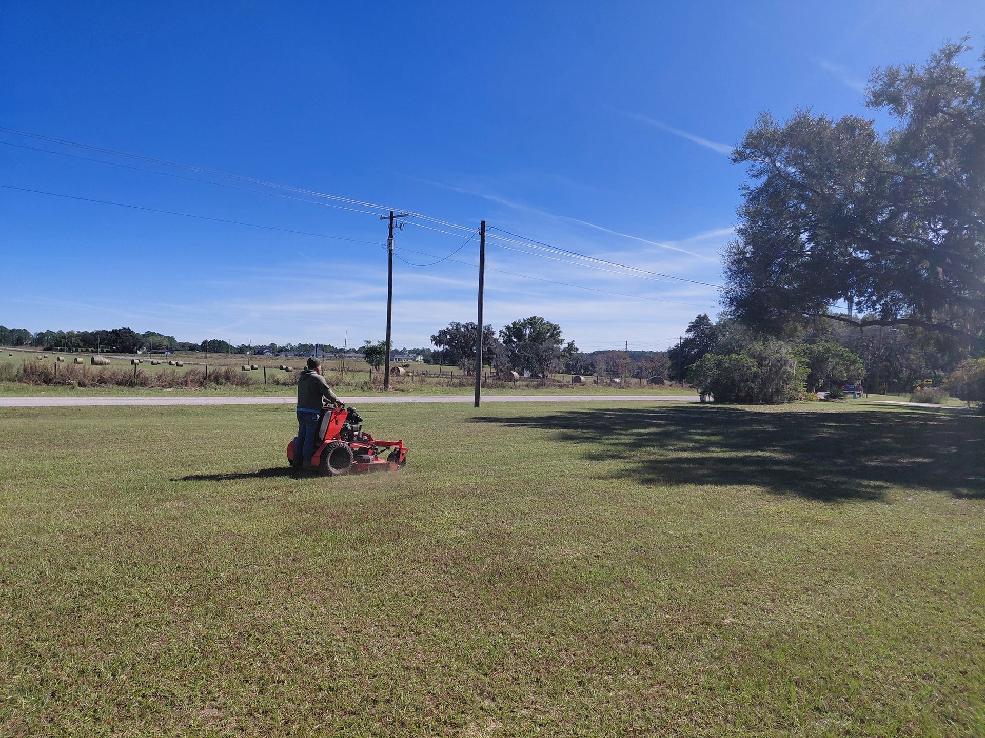 Person mowing a grassy field with a red tractor on a sunny day.