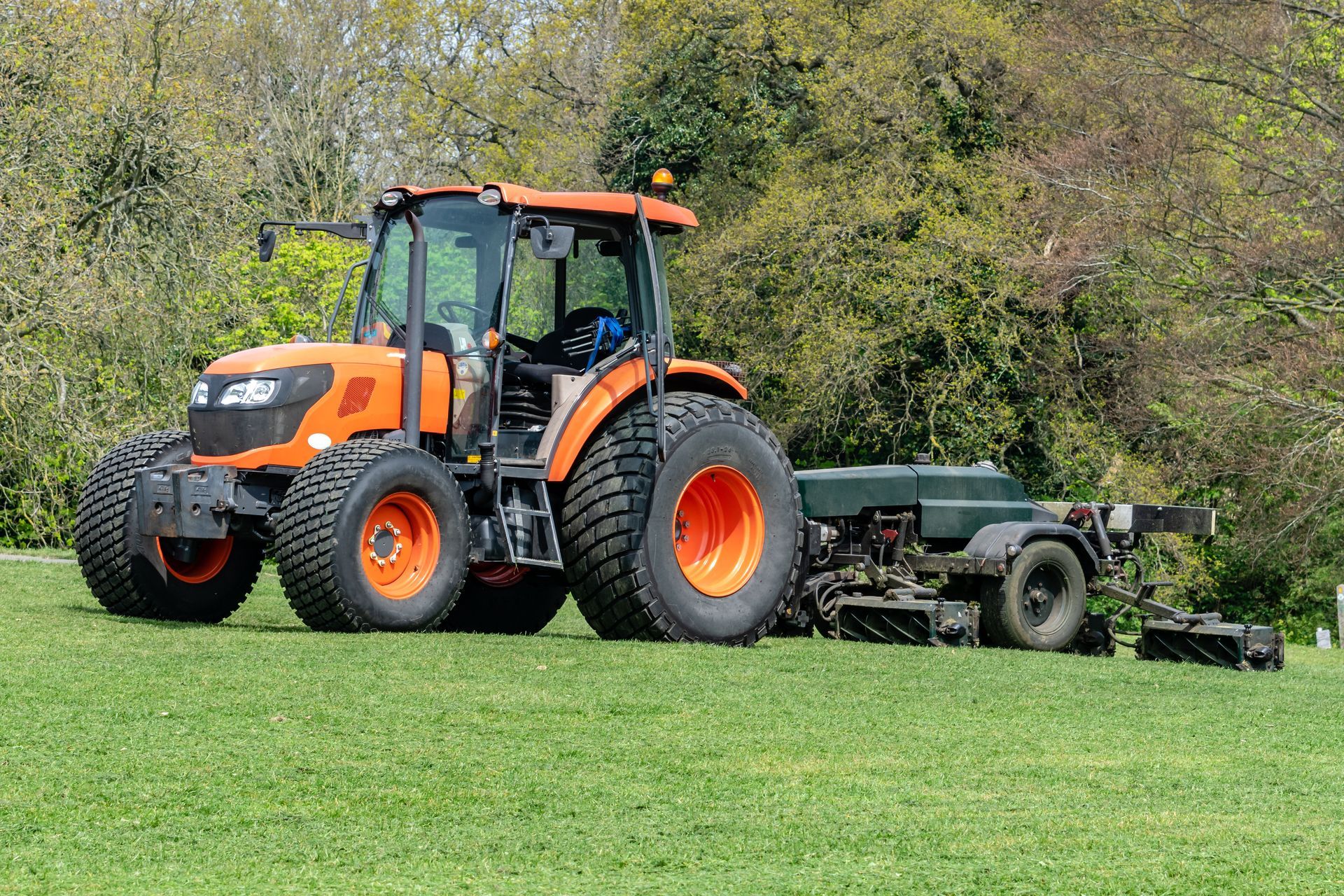 Orange tractor with attached implement on a green grassy field.