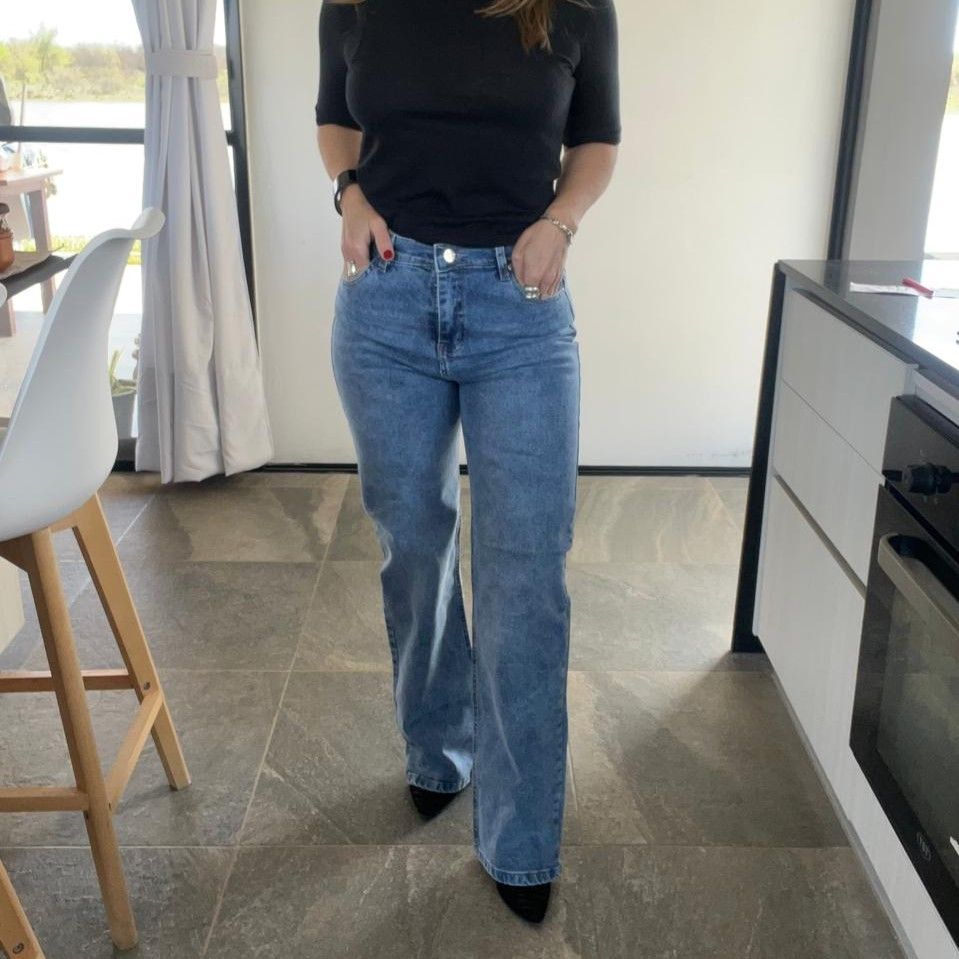 Mujer con top negro y jeans azules, manos en los bolsillos, en el interior.