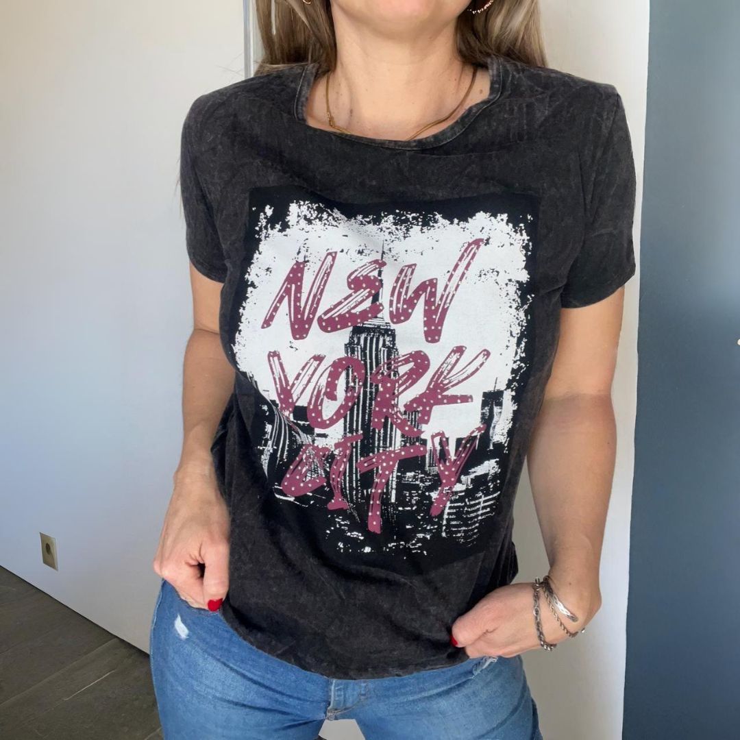 Mujer que viste una camiseta gris oscuro con el gráfico "New York City" y jeans azules.