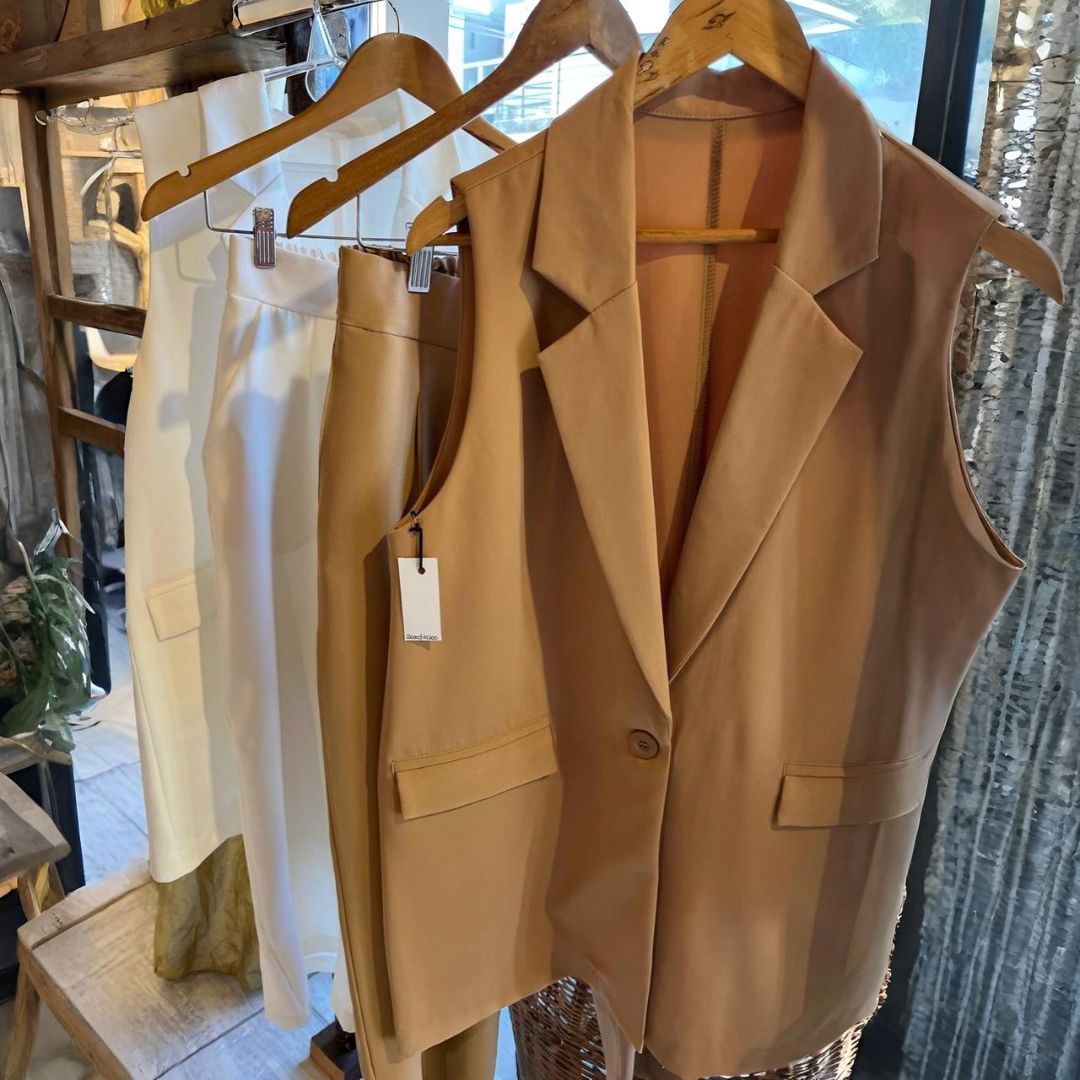 Mujer con chaleco y pantalones blancos, bufanda estampada, de pie en el interior.