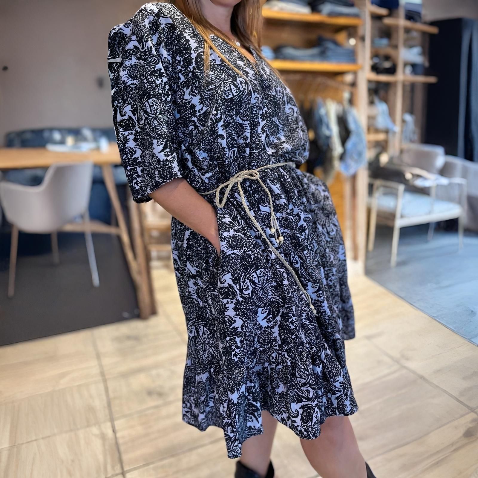 Mujer con un vestido floral negro y un cinturón de cuerda, de pie en el interior.