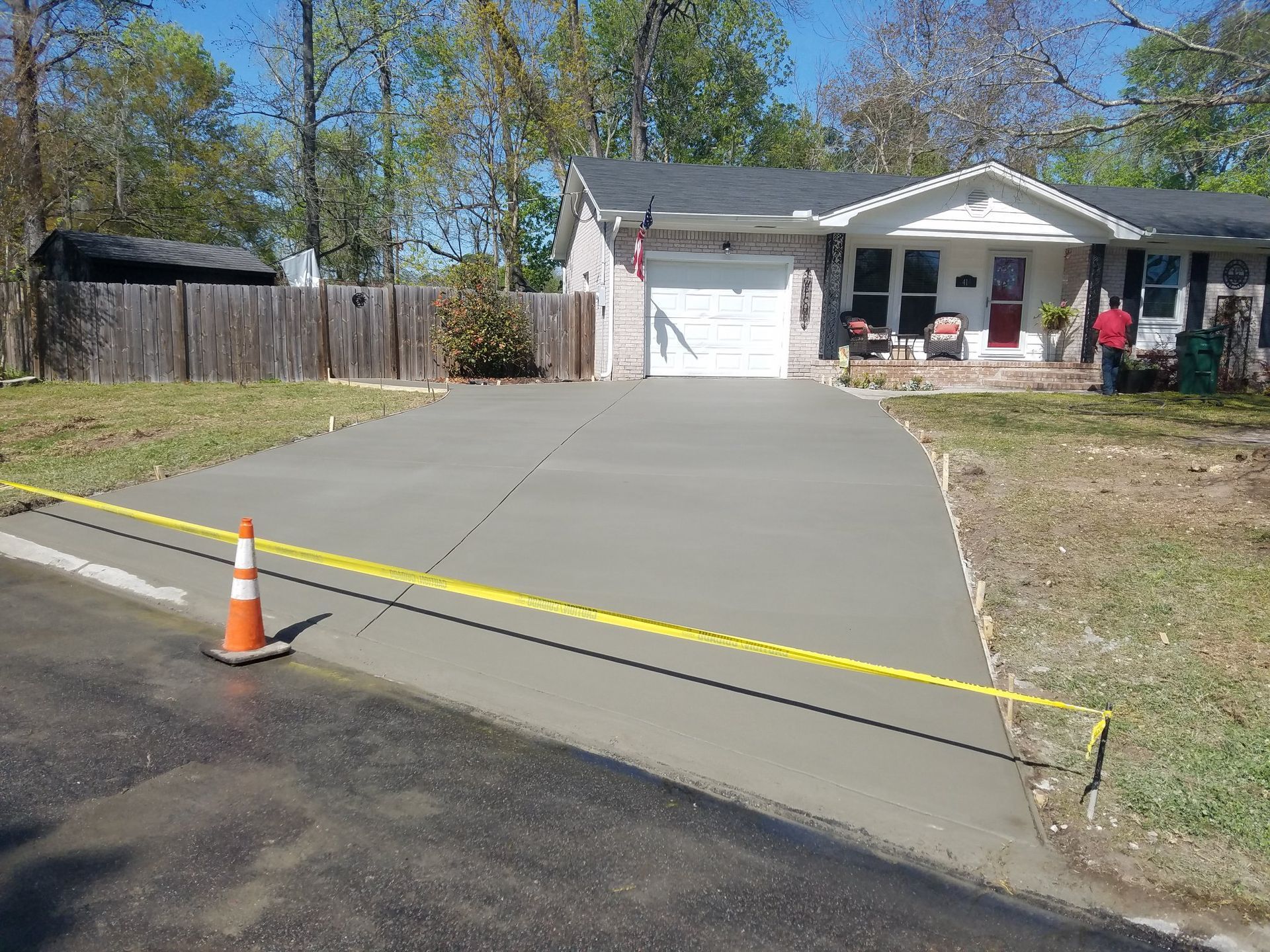 Freshly poured concrete driveway in front of a house, with yellow caution tape and an orange traffic cone.
