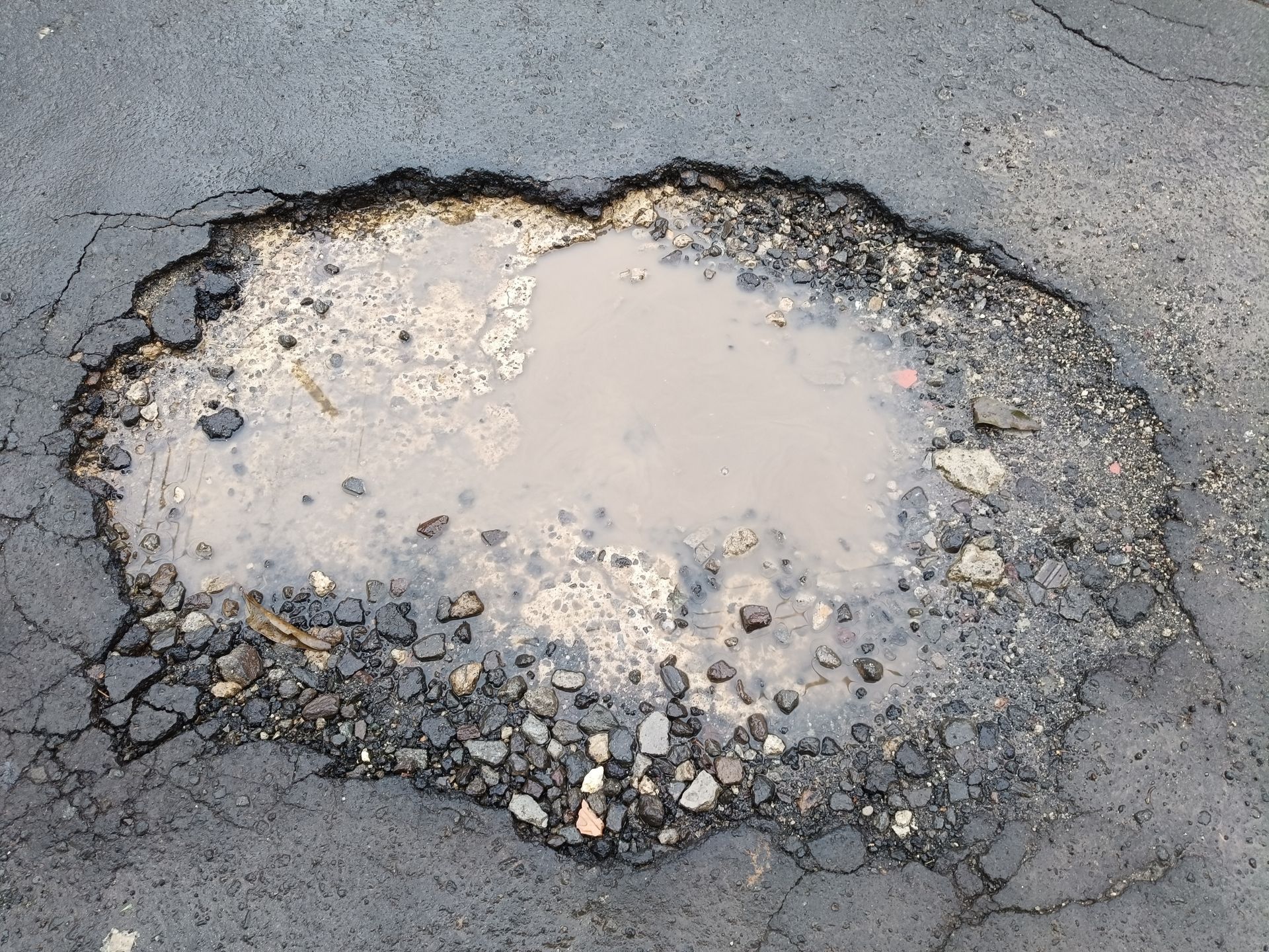 Pothole filled with murky water on asphalt road.