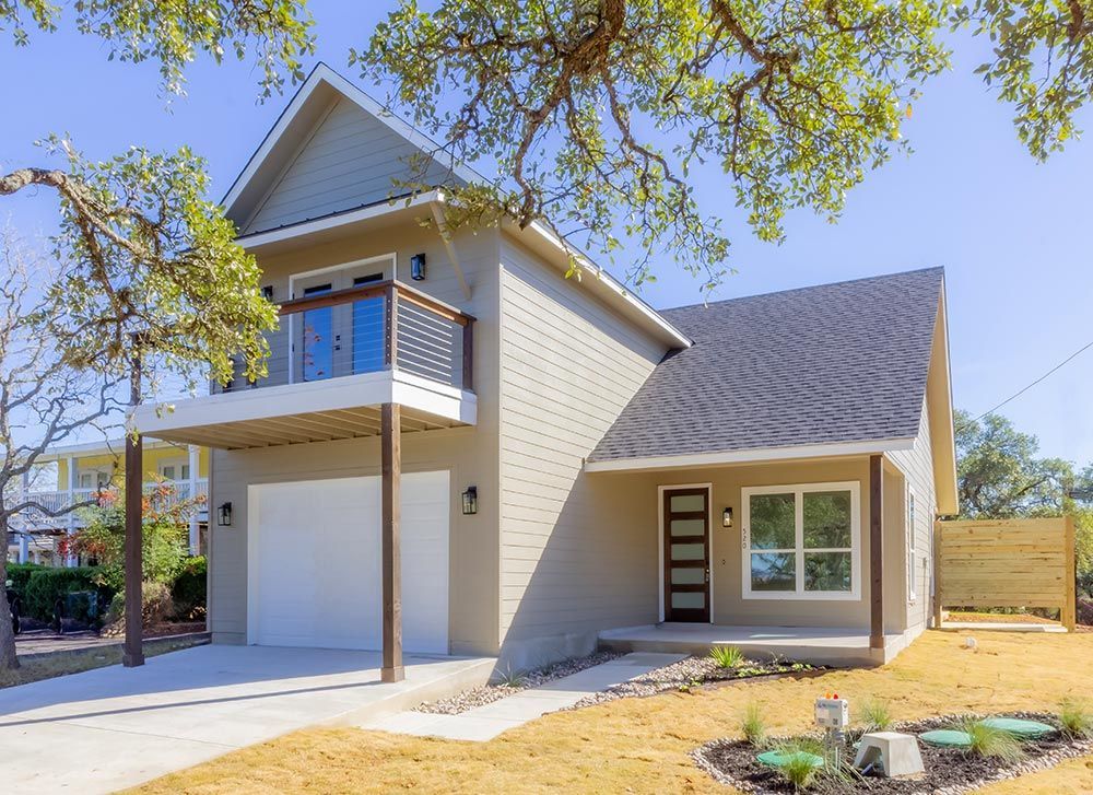 Modern two-story house with balcony, garage, and front entrance, with trees and lawn.