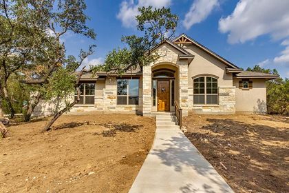 House exterior with tan stucco, stone accents, and a concrete path leading to a wood door.