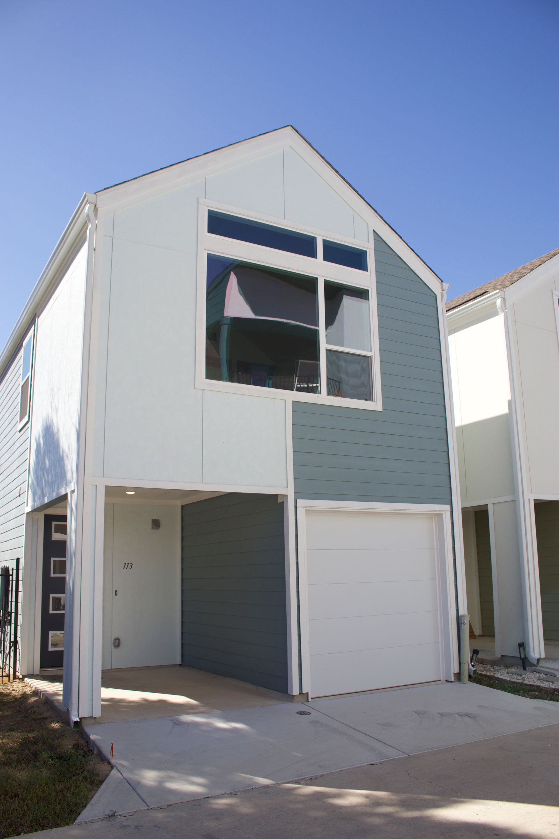 Modern two-story house with blue and white siding, garage, and large window on a sunny day.