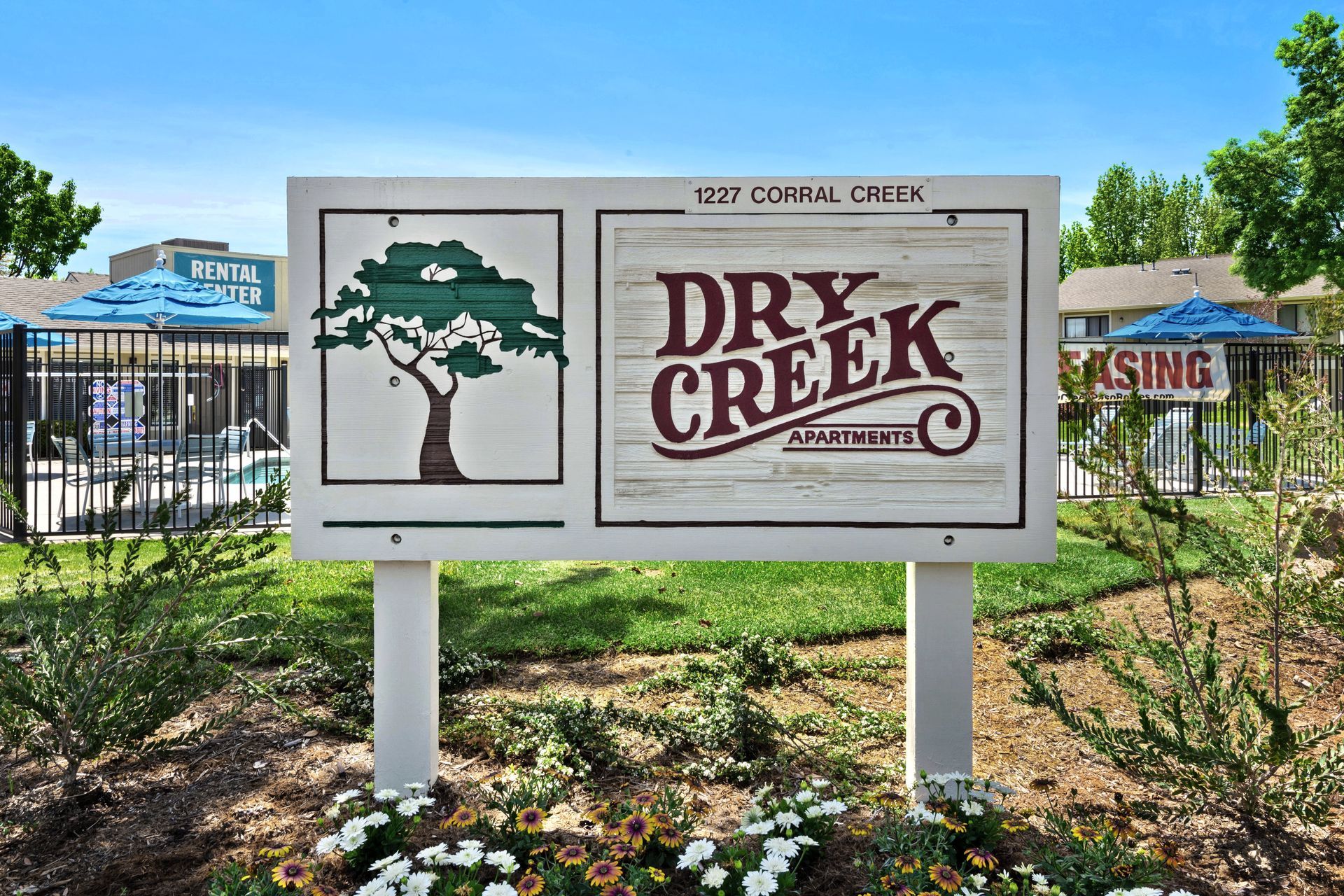 Sign for Dry Creek Apartments, brown and white, with a tree graphic and pool in the background.
